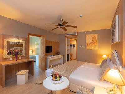 Světly hotelový pokoj s velkou postelí, stropním ventilátorem a útulným osvětlením.