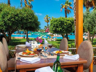 Elegantně prostřený stůl s jídlem a vínem, výhled na palmy a moře.