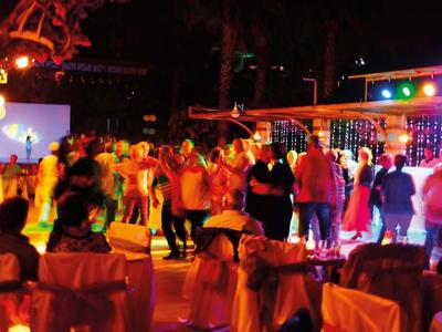 Persone che ballano all'aperto durante una festa serale con luci colorate.