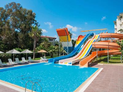 Parco acquatico con scivoli colorati accanto a una piscina in giardino d'hotel in una giornata di sole.