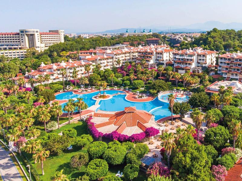 Velký hotelový resort s bazénem, barevnými květinami a obklopený bujnou zelení.