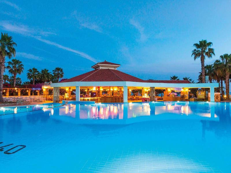 Osvětlený bazén před otevřeným pavilonem s palmami při západu slunce.