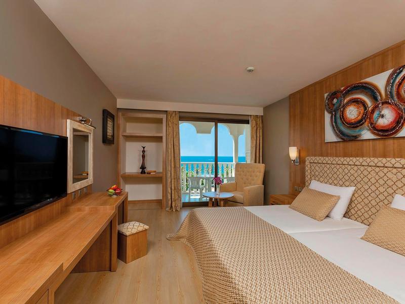 Moderní hotelový pokoj s manželskou postelí, TV, dřevěným dekorem a balkonem s výhledem na moře