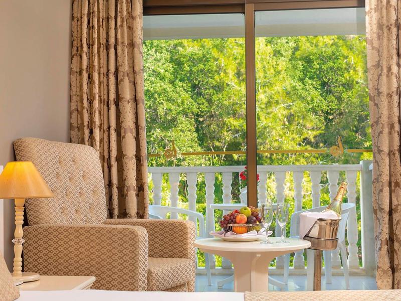 Pohodlné křeslo vedle stolu s ovocem před velkým oknem s výhledem na zelený balkon.