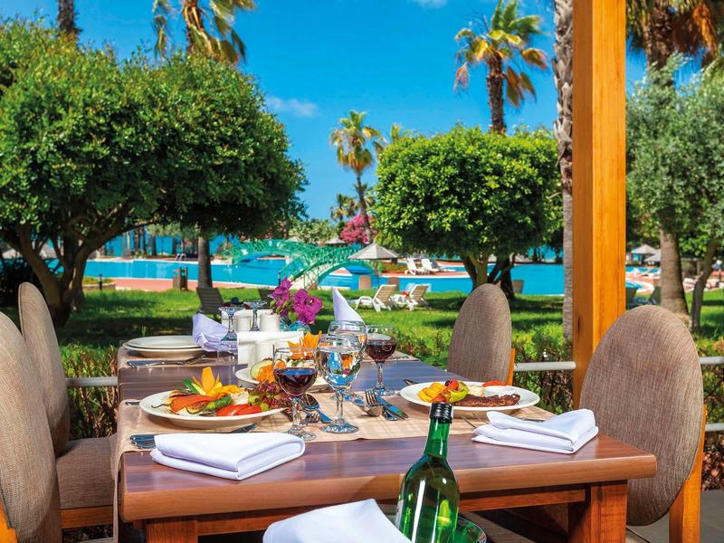 Elegantně prostřený stůl s jídlem a vínem, výhled na palmy a moře.