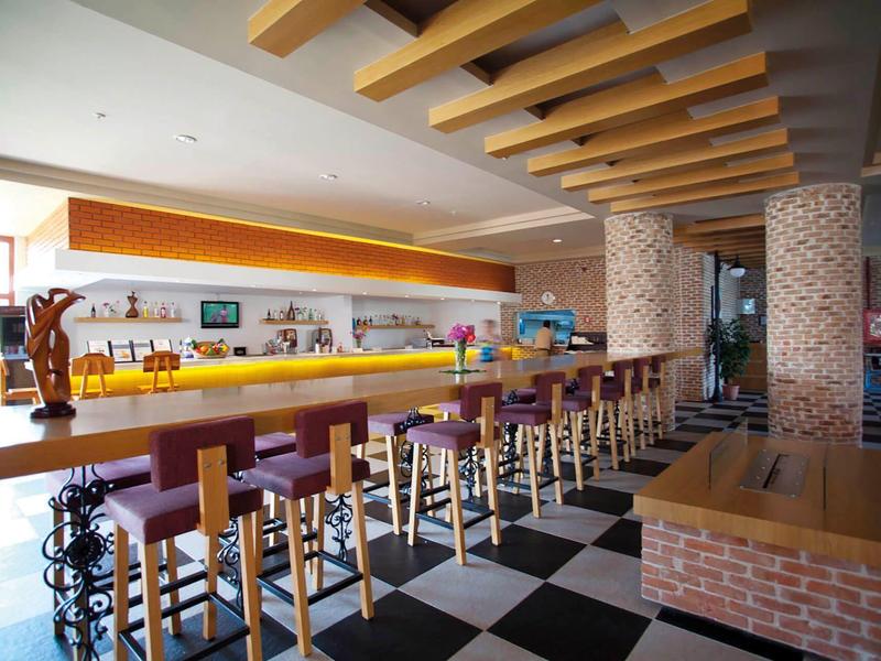 Moderní hotelový bar s vysokými dřevěnými židličkami a černo-bílou šachovnicovou podlahou.