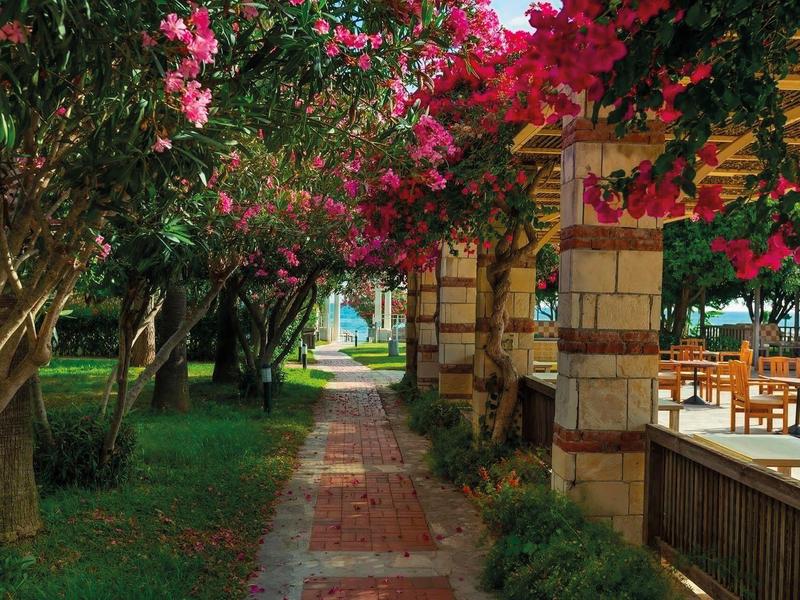 Cesta z červených kamenných dlaždic obklopená kvetoucími stromy a zastřešenými odpočívadly v zahradě.