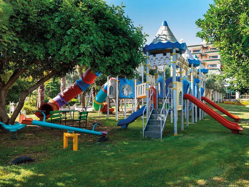 Barevné dětské hřiště s klouzačkami a prolézačkami v zeleném parku pod modrou oblohou.