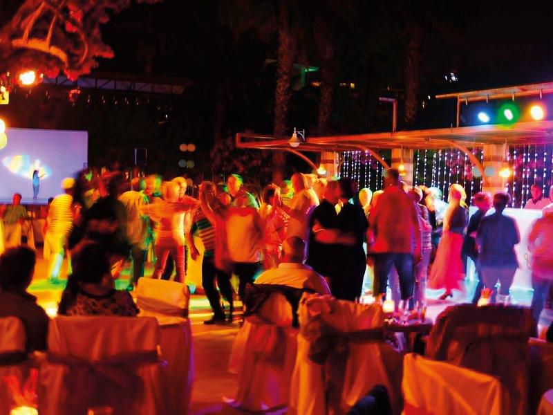 Lidé tančí na noční venkovní párty s barevnými světly.