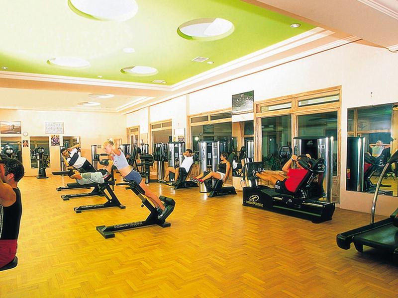 Světlá posilovna s různými tréninkovými stroji a lidmi cvičícími.