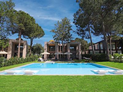 Nowoczesny basen hotelowy z leżakami, otoczony drzewami i budynkami w tle.