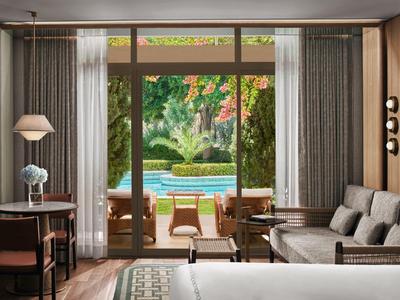 Blick durch große Fenster auf Terrasse mit Pool und grüner Gartenlandschaft im Hotelzimmer.