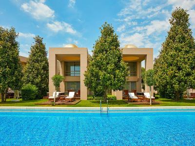 Moderner Hotelpool mit Liegestühlen und Bäumen auf der Wiese bei sonnigem Himmel.