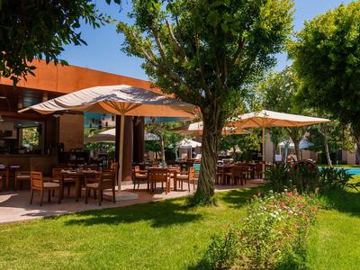 Buitengebied van een hotel met tafels, parasols en groen gazon onder bomen.