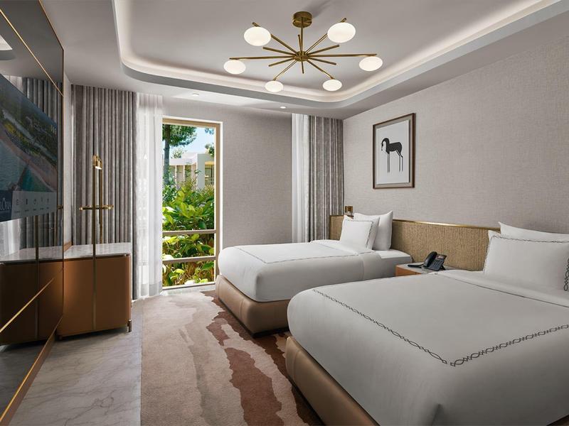 Modernes Hotelzimmer mit zwei großen Betten, großem Fenster und Balkon mit Blick ins Grüne.