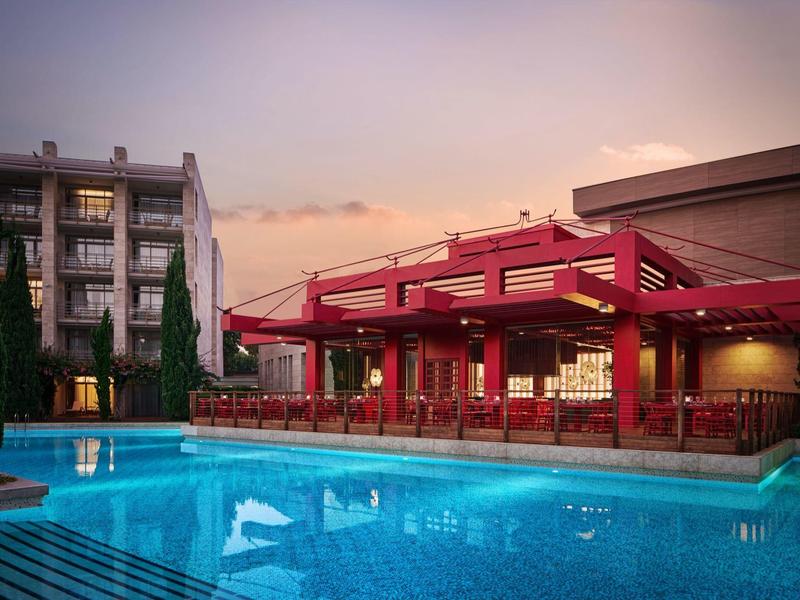Beleuchteter Außenpool mit rotem Pavillon und Hotelgebäude bei Sonnenuntergang.