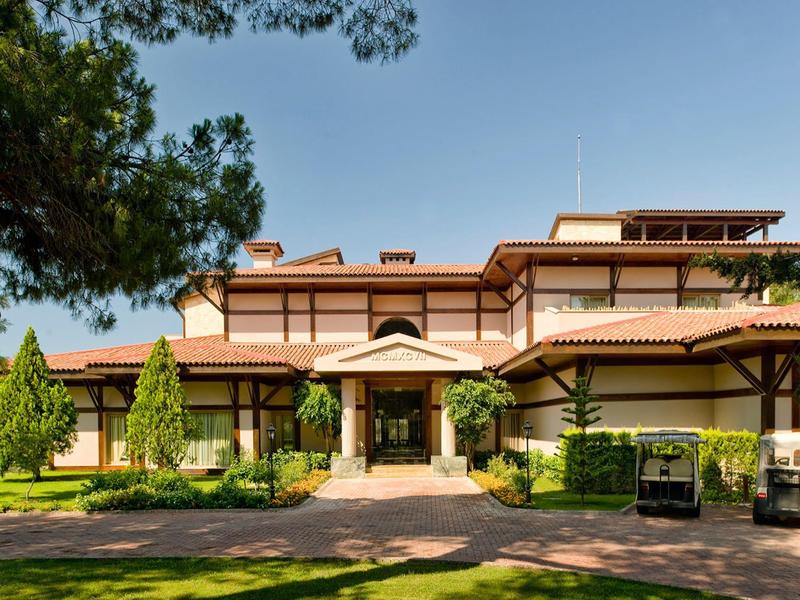 Ein großes Hotelgebäude mit rotem Dach, umgeben von Bäumen und einem gepflegten Garten.
