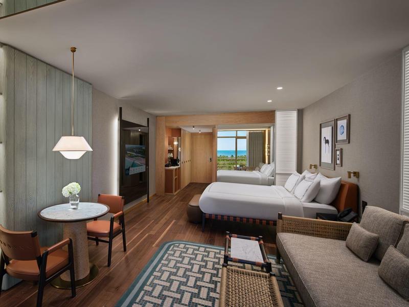 Modernes Hotelzimmer mit zwei Betten, Sitzbereich, Esstisch und Blick auf das Meer.