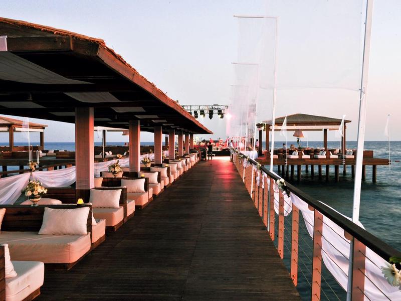 Breiter Steg mit Sitzbereichen und Blick auf das Meer bei Sonnenuntergang