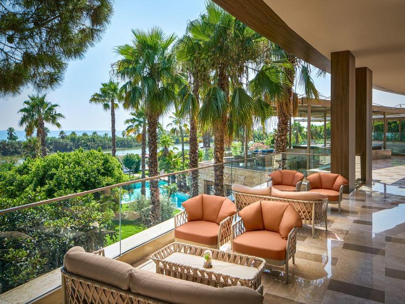 Terrasse mit gemütlichen Sitzgelegenheiten und Blick auf Palmen und Pool im Hotel