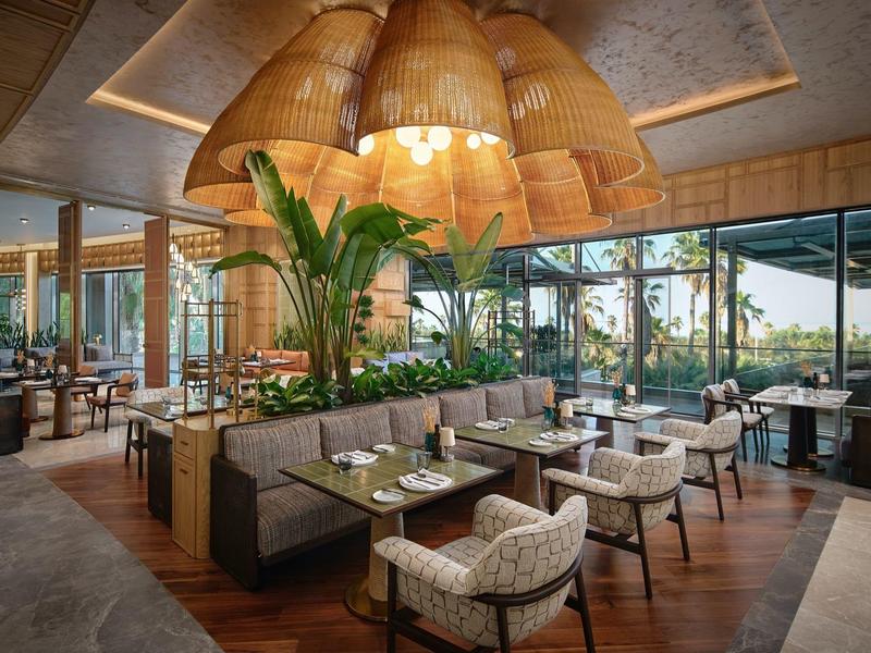 Moderner Hotelrestaurantbereich mit hängenden Korblampen und Panoramafenstern mit Gartenblick.