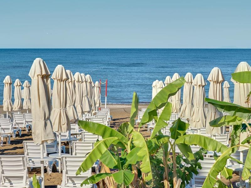 Zone de plage fermée avec mobilier blanc et feuillage vert au bord de la mer.