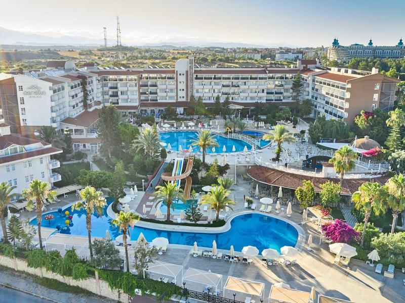 Grand complexe hôtelier avec plusieurs piscines entourées de palmiers et de plantes en fleurs.