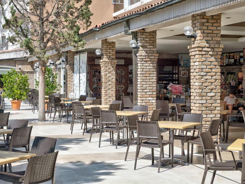 Espace café extérieur avec colonnes en pierre et plusieurs chaises et tables sous un auvent.