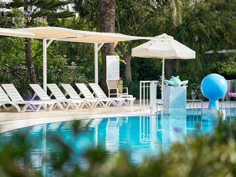 Espace piscine avec chaises longues, parasols et piscine bleue claire dans un hôtel tropical.