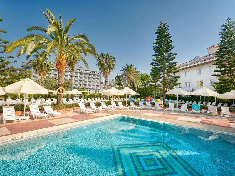 Piscine d'hôtel avec chaises longues et parasols dans un cadre tropical sous un ciel ensoleillé.