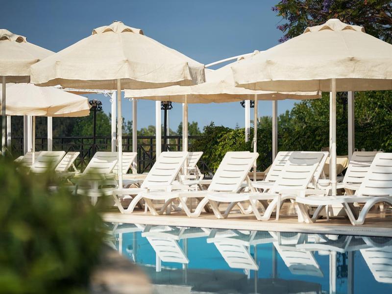 Chaises longues blanches et grands parasols au bord de la piscine sous un ciel bleu clair.