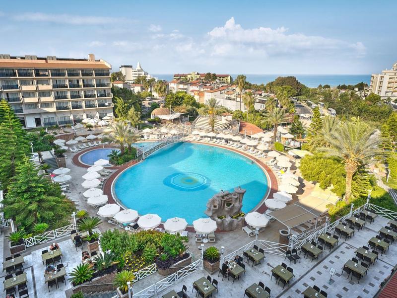Grande piscine d'hôtel avec parasols et transats dans un jardin près de la mer.