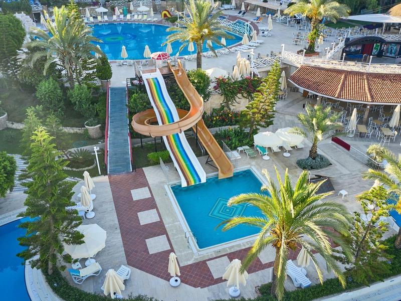 Parc aquatique avec toboggans colorés, piscines et palmiers dans une station hôtelière.