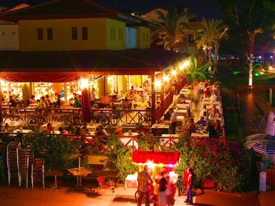 Restaurant extérieur éclairé dans un hôtel tropical la nuit avec de nombreux clients.