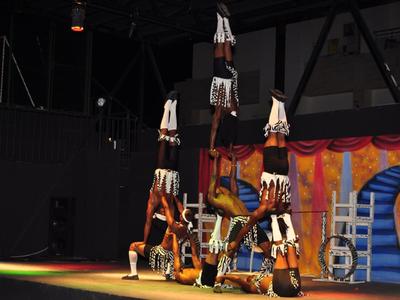 Mehrere Akrobaten bilden eine menschliche Pyramide auf einer Bühne mit farbiger Kulisse.