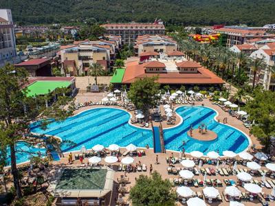 Grande piscina dell'hotel con ombrelloni e lettini, circondata da edifici e montagne verdi.
