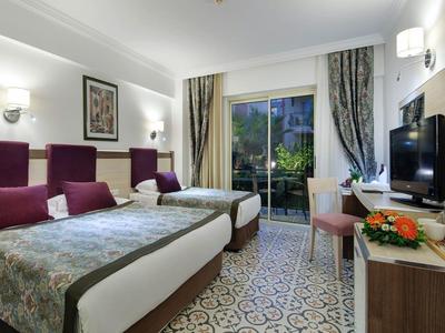 Chambre d'hôtel moderne avec deux lits doubles, TV, bureau et balcon surplombant la verdure.