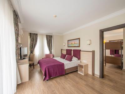 Chambre d'hôtel lumineuse avec lit double, couvre-lit violet, chaise et bureau à côté d'une grande fenêtre.