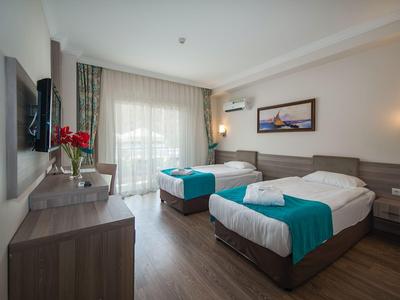 Hotelzimmer mit zwei Einzelbetten, Holzmöbeln und großen Fenstern mit Vorhängen.