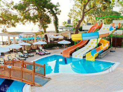 Piscine pour enfants avec toboggans colorés, un pont et des tables avec parasols à côté d'une piscine plus grande.
