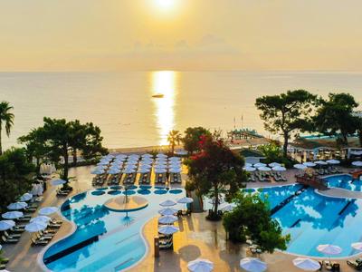 Sonnenuntergang über einem Poolbereich mit Liegestühlen und Bäumen am Meer.