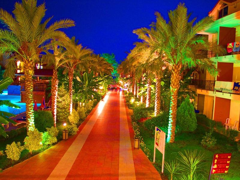 Chemin éclairé avec des palmiers entre les bâtiments de l'hôtel la nuit