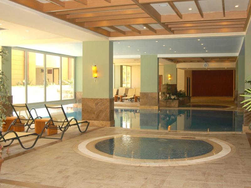 Piscine intérieure avec jacuzzi et sièges dans une zone d'hôtel moderne.