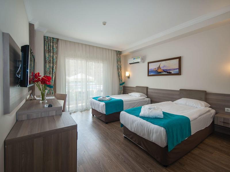 Chambre d'hôtel avec deux lits, bureau, télévision et balcon avec rideaux.