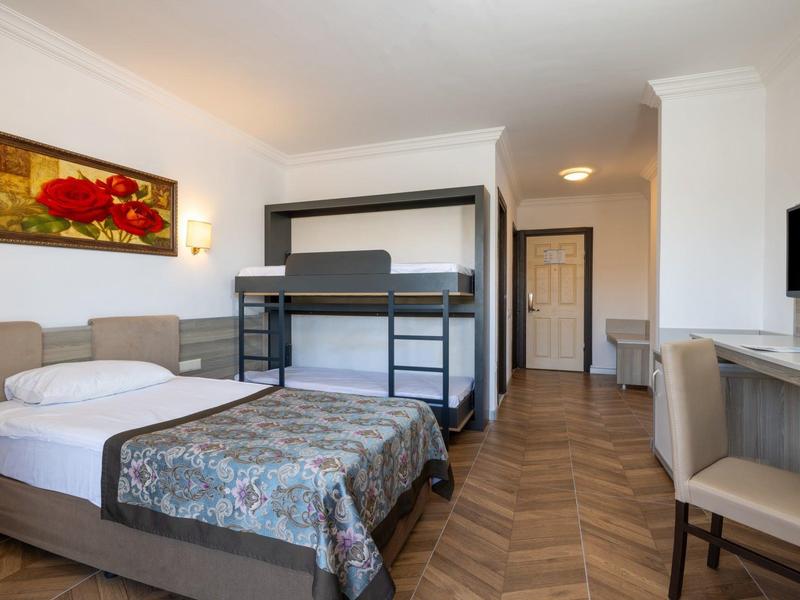 Chambre d'hôtel avec lit simple, lit superposé, bureau et télévision, décor moderne.