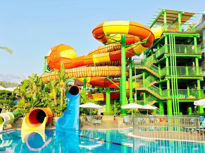 Parc de toboggans aquatiques coloré à côté d'un hôtel avec piscine et parasols.