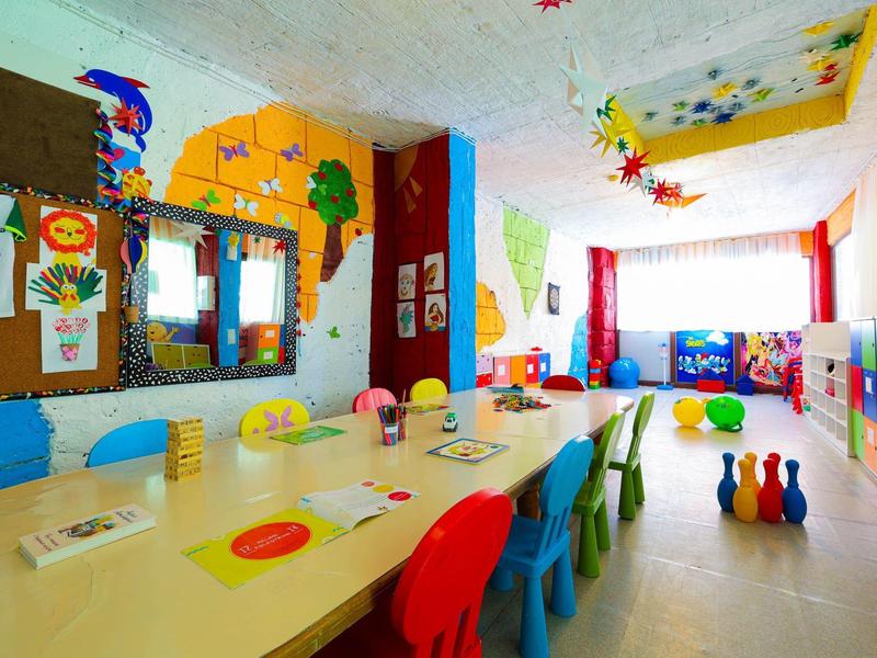 Salle de jeux colorée pour enfants avec une table et des chaises multicolores dans une pièce lumineuse.