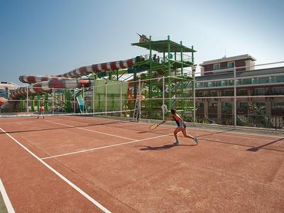 Woman and child relax by large hotel pool with sun umbrellas and modern buildings in background.