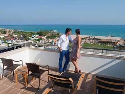 Pár si užívá výhled na moře z hotelové terasy s křesly.