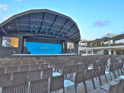 Prázdné otevřené kino s pódiem a řadami sedadel pod modrou oblohou.